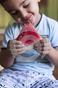 Kid eats fruit in the kitchen. A little boy holding a slice of water melon. happy boy kid eating watermelon