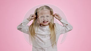 Kid emotional outburst. Angry girl screaming and gesturing with fists, expressing negative emotions, pink background