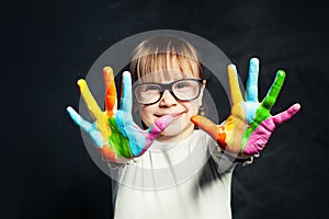 Kid enjoying his painting. Cute child girl with colorful hands on classroom blackboard background. Arts and creative education