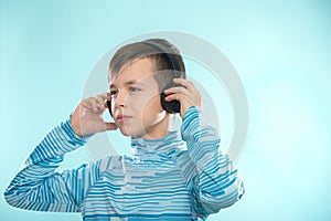 Kid enjoying music on his headphones, listening to music. Handsome young stylish kid in headphones standing against blue backgroun