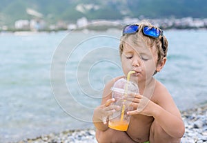 Kid with enjoyment drink juice through a tube on sea beach