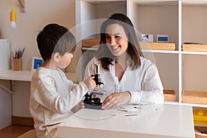 Kid exploring science with a microscope and mother or teacher help. Homeshooling. Learning Community. Montessori School