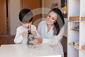 Kid exploring science with a microscope and mother or teacher help. Homeshooling. Learning Community. Montessori School