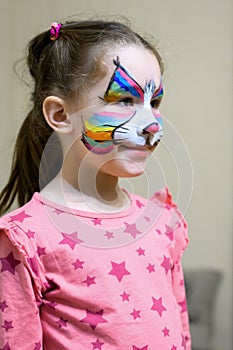 Kid with face painting of kitty, cute little girl with painted mask on her face of rainbow cat