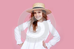 Kid fashion model on a pink background, kid portrait, girl in a white romantic dress and straw hat, kid model in studio.