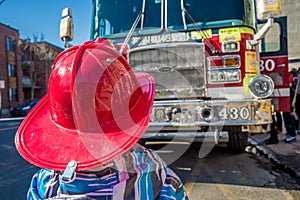 Kid with a fire fighter helmet in front of a fire truck