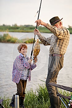 Kid fishing in lake with grandfather. cath a fish with fishing rod, happy and excited