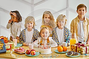 kid friends with birthday cake on table and looking at camera