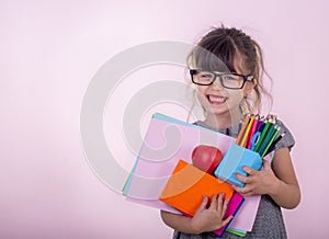 Kid gets ready for school. Schoolgirl holding many school supplies: pens, notebooks, scissors and apple. Back to school concept.