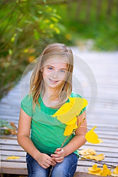 Kid girl in autumn wood deck with yellow leaves outdoor