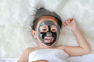 Kid girl in black peeling face mask, beauty concept