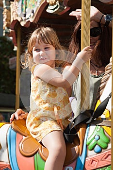 Kid girl in carousel horse next to woman