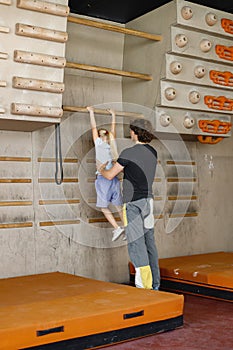 Kid girl at climbing wall with male instructor in climbing center