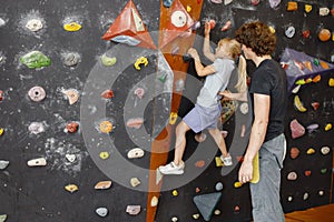 Kid girl at climbing wall with male instructor in climbing center