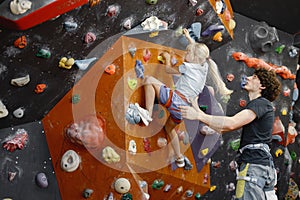 Kid girl at climbing wall with male instructor in climbing center