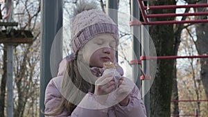 Kid girl eating fast food outdoors. Unhealthy nutrition of schoolchildren