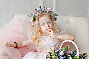 Kid - girl in a flower crown. Beautiful little girl in a bright studio sits, and looks into the camera near basket of