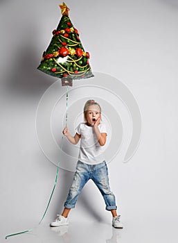 Kid girl in full growth with christmas tree air balloon is awing, surprised, excited on white with free copy space.