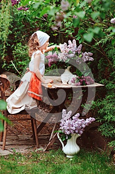 Kid girl at garden tea party in spring day with bouquet of lilacs syringa