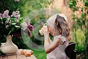 Kid girl at garden tea party in spring day with bouquet of lilacs syringa