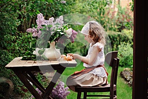 Kid girl at garden tea party in spring day with bouquet of lilacs syringa