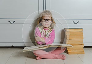 Kid girl with glasses and a stack of books sitting on the floor