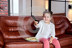 Kid girl is going to eat hamburger and watch tv, sitting on sofa in living room