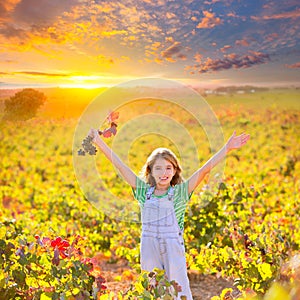 Kid girl in happy autumn vineyard field open arms red grapes bun