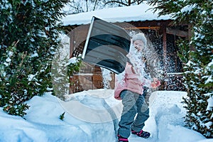 Kid girl helping to clean pathway from snow with shovel.