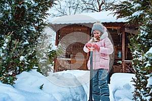 Kid girl helping to clean pathway from snow with showel.