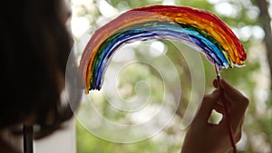 Kid girl at home on the window draws a rainbow during coronavirus Covid-19 the quarantine period on self-isolation. Stay