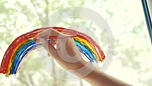 Kid girl at home on the window draws a rainbow during coronavirus Covid-19 the quarantine period on self-isolation. Stay