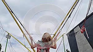 a kid girl jumps on a bungee trampoline. entertainment for children in park.