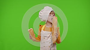 Kid girl kid dressed in apron and hat like chef cook eating fresh tasty baguette, fooling around