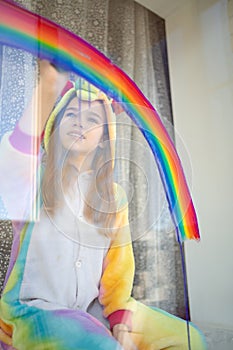 Kid girl in kigurumi draws rainbow on window. photo