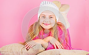 Kid girl knitted hat. Winter accessory concept. Girl long hair dream pink background. Kid dreamy lean on pillows. Winter