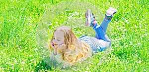 Kid girl laying at green grass at spring time. Peace and tranquil concept. Girl on smiling face spend leisure outdoors