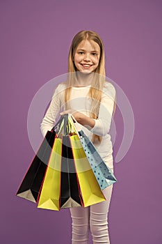 Kid girl with long hair fond of shopping. Girl on smiling face carries bunches of shopping bags, isolated on white