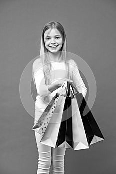 Kid girl with long hair fond of shopping. Girl on smiling face carries bunches of shopping bags, isolated on white