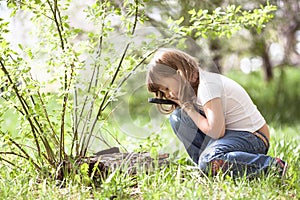 Kid girl with magnifying glass explores grass