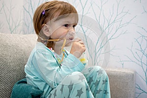 Kid girl makes inhalation with a nebulizer. sick child holding inhalator in hand and breathes through an inhaler at home