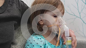 Kid girl makes inhalation with a nebulizer. sick child with mother holding inhalator in hand and breathes through an inhaler at