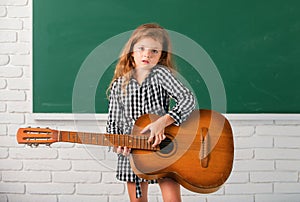 Kid girl on musik lesson at school. Elementary school child hold guitar in class.