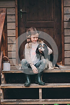 Kid girl playing with her spaniel dog, sitting on stairs at wooden log cabin