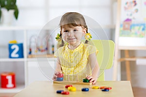 Kid girl playing with logical toy on desk in nursery room or kindergarten. Child arranging and sorting colors and sizes