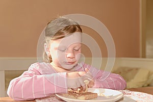 Kid girl playlful eats chocolate cream spread on bread. Chocolate sweet food snack. Happy girl has a snack in the