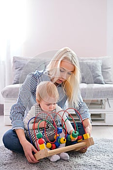 Kid girl plays with educational toy indoor. Happy mother looking at her smart daughter