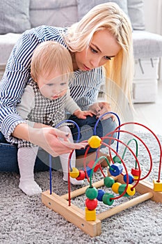 Kid girl plays with educational toy indoor. Happy mother looking at her smart daughter