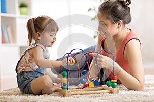 Kid girl plays with educational toy in nursery at home. Happy mother looking at her smart daughter.