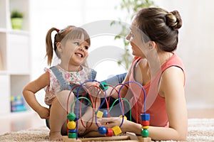 Kid girl plays with educational toy in nursery at home. Happy mother looking at her smart daughter.